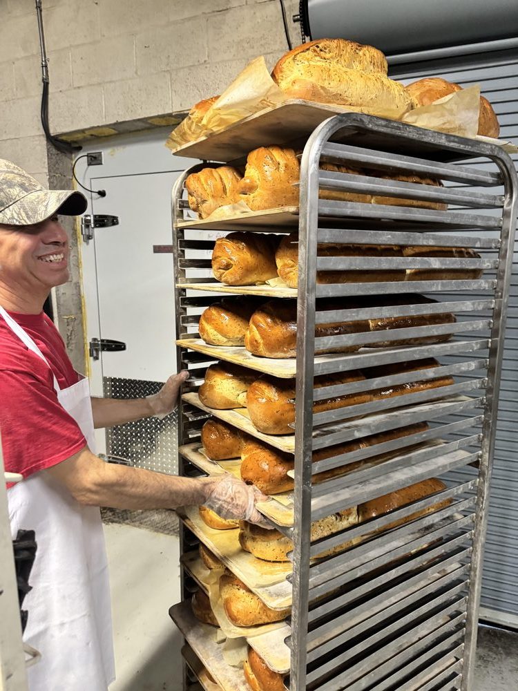 A baker pulling a rack of fresh bread out of the oven