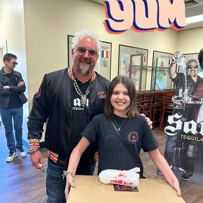 Guy Fieri posing with a young NYBB fan holding a takeout box