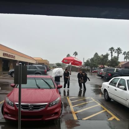 Customers walking through the rainy parking lot under an NYBB umbrella